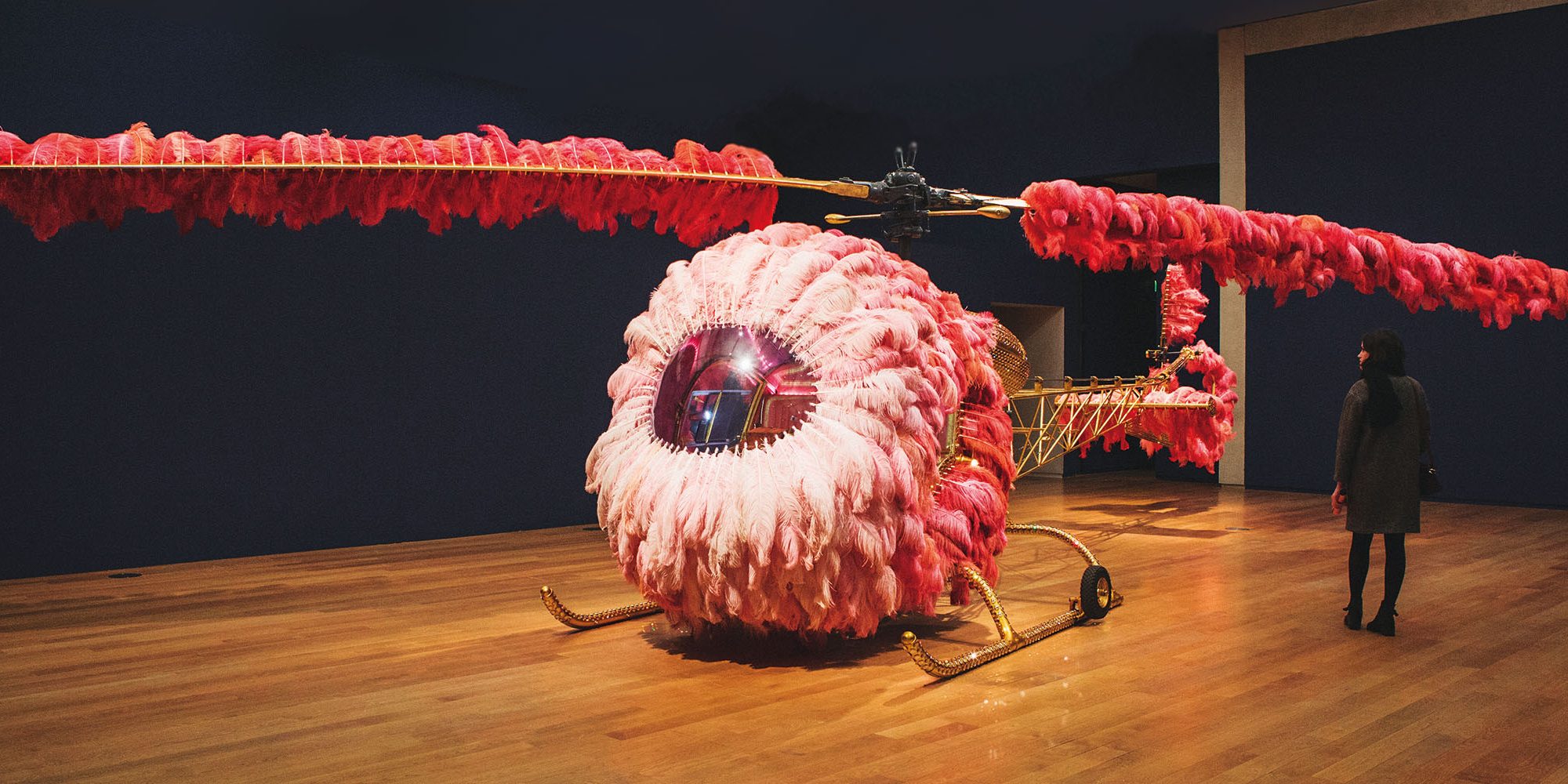 Woman looking at artwork, gold helicopter covered in pink feathers