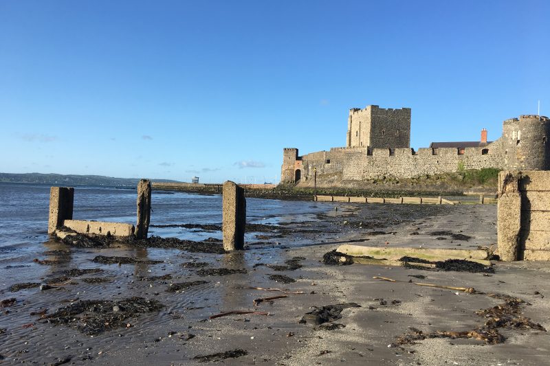 Walled castle sits on a beach, tide partly out, seaweed visible on sand