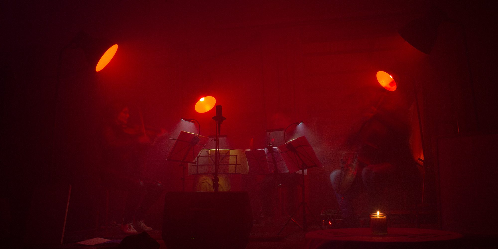 Four members of a chamber orchestra sit in semi circle under four red spot lights